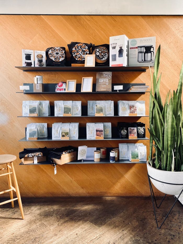 gallery-5 Neatly organized coffee shop shelves featuring products, decor, and a potted plant against a wooden backdrop.