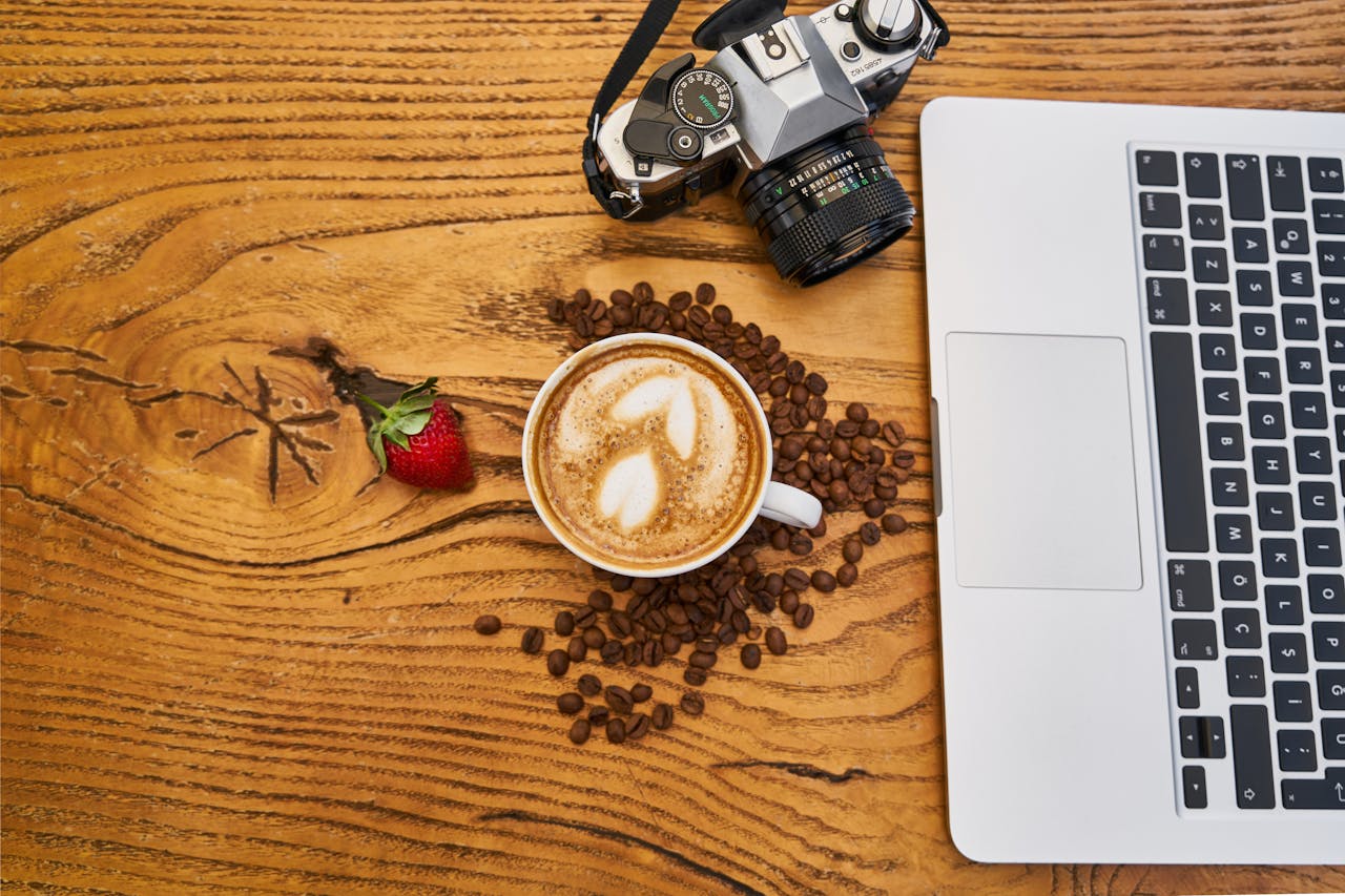 services-img A creative flatlay with coffee, camera, strawberry, and laptop on wooden surface.