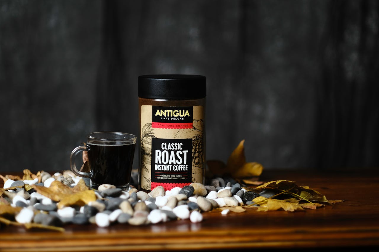 gallery-2 A still life of Antigua Classic Roast Instant Coffee with autumn leaves and pebbles.