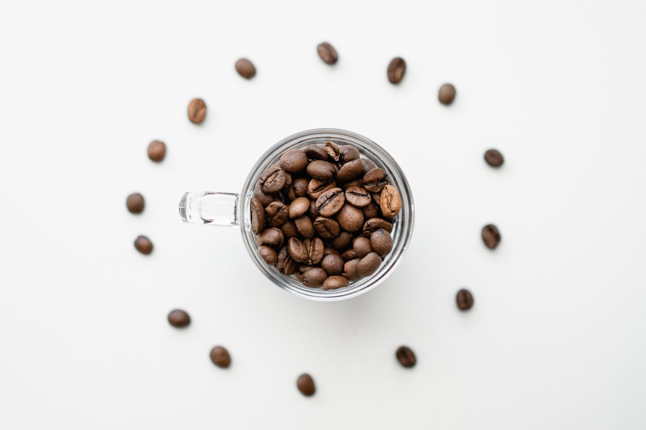 services-02 Artistic top shot of coffee beans in a glass mug, arranged in a circle on a white surface.