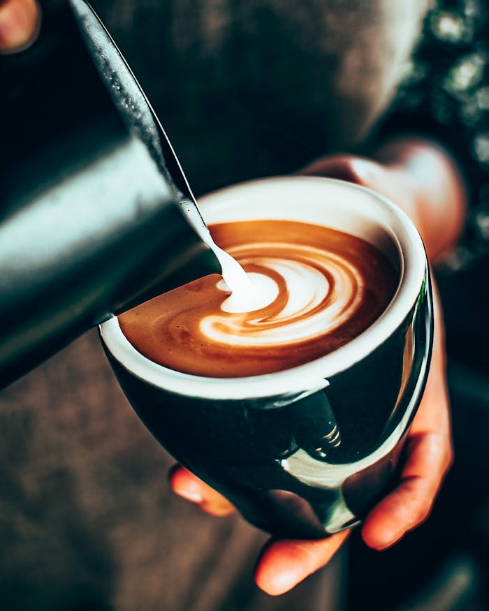 A barista skillfully pouring milk into a coffee cup, creating intricate latte art.