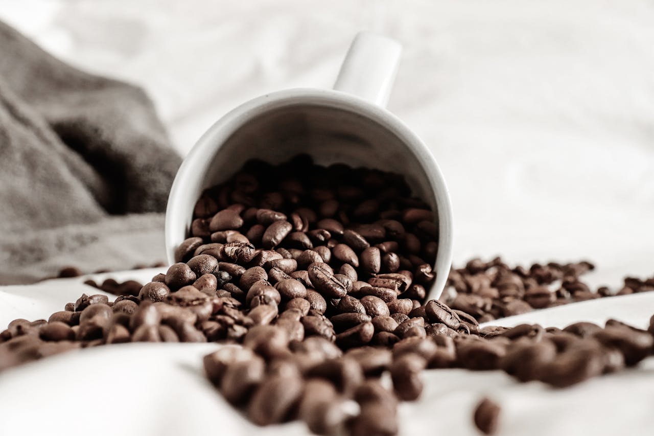 Aromatic coffee grains scattered on white cloth from fallen ceramic cup against plaid